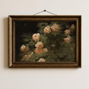 Puede incluir: Pintura al óleo de un rosal en plena floración, con rosas de color melocotón claro sobre un fondo verde oscuro. La obra de arte está enmarcada en un marco de madera dorado y adornado, colgada por un alambre negro.