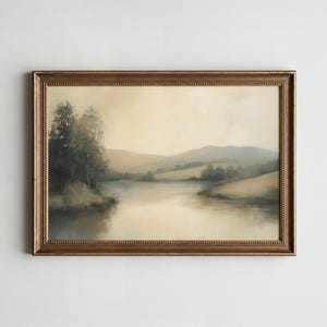 Könnte beinhalten: Gerahmtes Landschaftsgemälde, das eine ruhige Seeszene darstellt. Das Kunstwerk weist eine gedämpfte Farbpalette mit Beige-, Grün- und Grautönen auf. Das Gemälde ist in einem dekorativen goldfarbenen Rahmen eingefasst, der seine Vintage-Ästhetik unterstreicht.