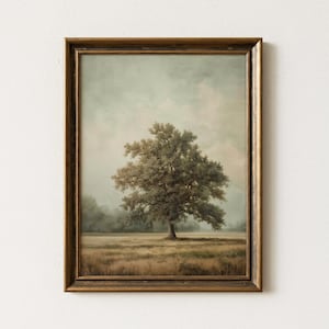 Op de afbeelding: Een ingelijst landschapsschilderij met een grote boom in een veld. Het kunstwerk heeft een vintage esthetiek met gedempte kleuren, waaronder tinten bruin, groen en grijs. De lijst is donker en sierlijk goudkleurig.