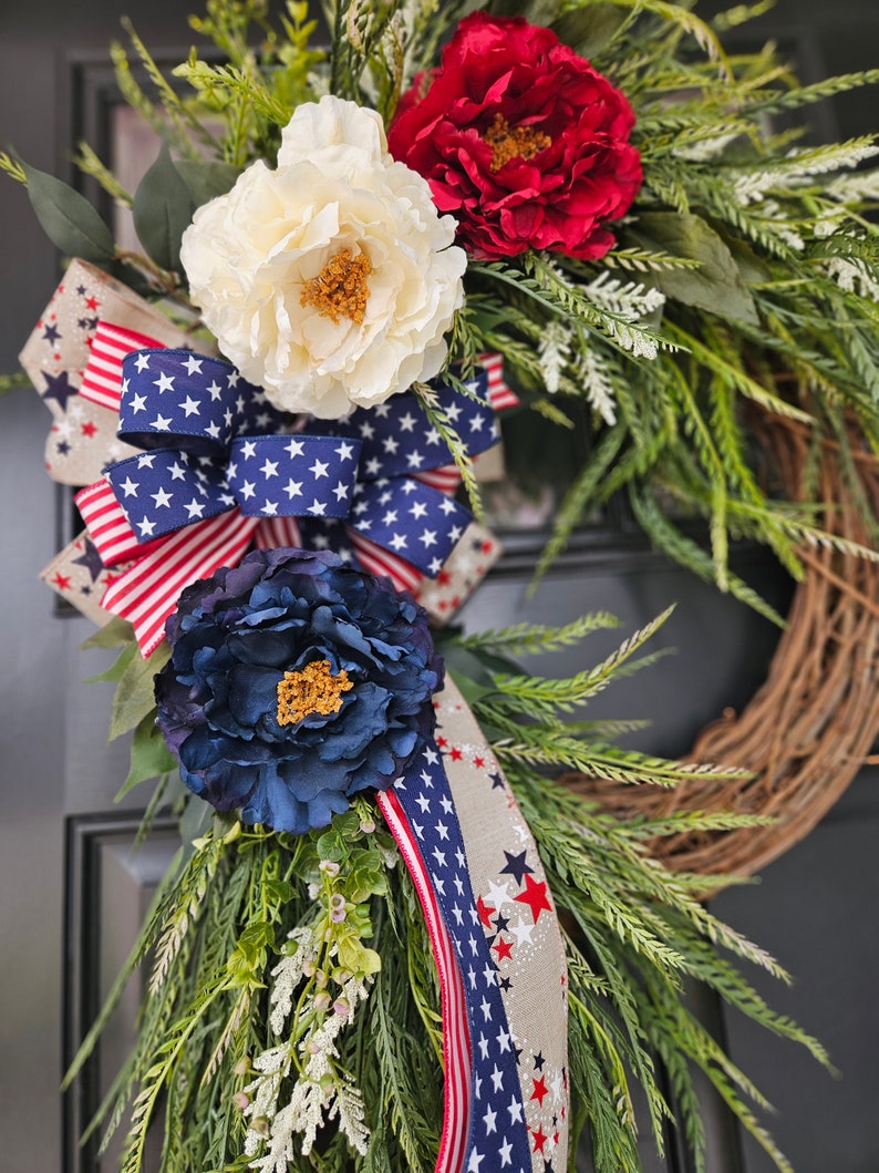 May include: A patriotic wreath with red, white, and blue flowers and a ribbon with stars. The wreath is made of twigs and has a green base.