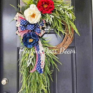 May include: A patriotic wreath with red, white, and blue flowers and a star-spangled ribbon. The wreath is made of twigs and has a green leafy base. The text "Pristine Door Decor" is visible in the bottom center of the image.