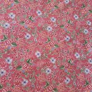 May include: A pink fabric with a floral pattern. The pattern features small pink, blue, and yellow flowers with green leaves.