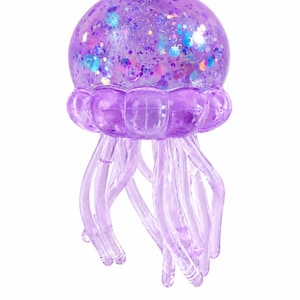 May include: A translucent purple jellyfish figurine featuring a rounded bell filled with iridescent, multi-colored glitter and sequins. The creature has a segmented lower bell section and several long, smooth, dangling tentacles extending downward.