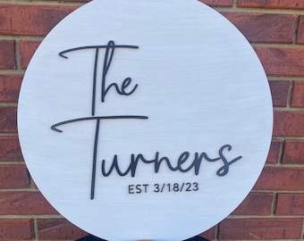 May include: White round wooden sign with black lettering that reads "The Turners EST 3/18/23". The sign is sitting on a small wooden slice with the words "True Love Designs" carved into it.