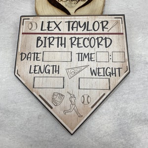 以下が含まれることがあります： 「LEX TAYLOR BIRTH RECORD」と書かれた木製ベースボール型のサイン。日付、時間、身長、体重を記入するスペースがあります。