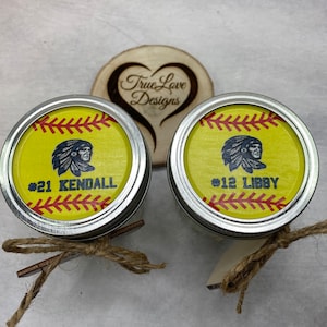 Puede incluir: Dos tapas de tarro Mason personalizadas con tem&aacute;tica de softbol con bordes plateados. Las tapas presentan un fondo amarillo con costuras rojas, un gr&aacute;fico nativo americano y los nombres "KENDALL" y "LIBBY" con sus n&uacute;meros. Atadas con hilo.