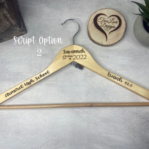 May include: A wooden clothes hanger with engraved text. The hanger has the words "Savannah Class of 2022", "Armorel High School", and "Isaiah 43:2". The hanger is light brown with a silver hook.