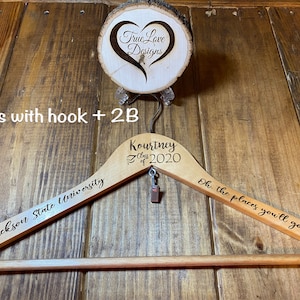 May include: A wooden clothes hanger with engraved text, including "Jackson State University" and "Kourtney Class of 2020." The hanger also features the phrase "Oh, the places you'll go!" and a small charm. A wooden disc with "True Love Designs" is above.
