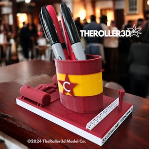 May include: A red and yellow 3D printed pen holder shaped like a ship's smokestack. The holder has a red star with a white "C" in the center and the text "SS EDMOND FITZGERALD" on the side. The text "THERoller3D 46™" is visible in the background.