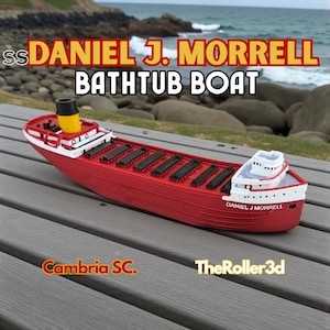 May include: A red and white toy boat with the text "DANIEL J. MORRELL BATHTUB BOAT". The boat has a yellow smokestack and black cargo hatches. The boat is sitting on a gray surface.