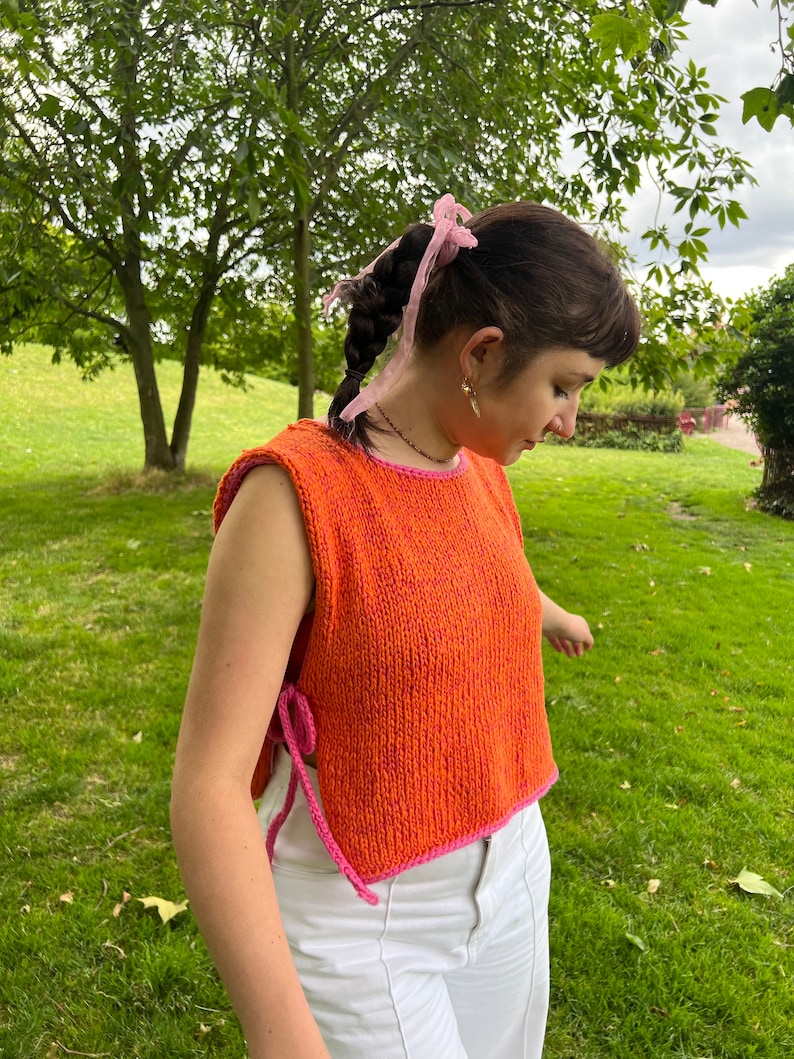 May include: A sleeveless knitted top in orange and pink with a pink ribbon in the woman's hair.