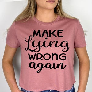 May include: A mauve cropped t-shirt with the text "Make Lying Wrong Again" printed in black.