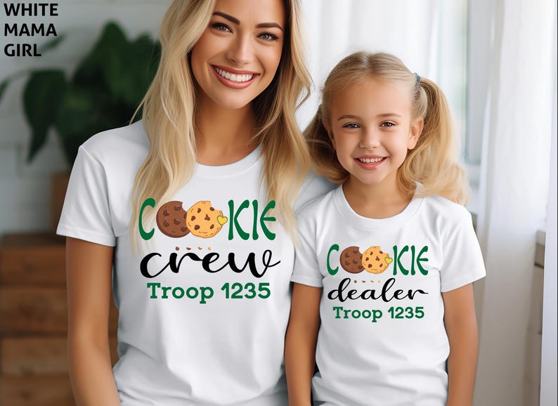 May include: White t-shirts with matching designs. One shirt says "COOKIE crew" and the other says "COOKIE dealer". Both shirts have a cookie graphic and "Troop 1235" in green. The shirts are for a mother and daughter.