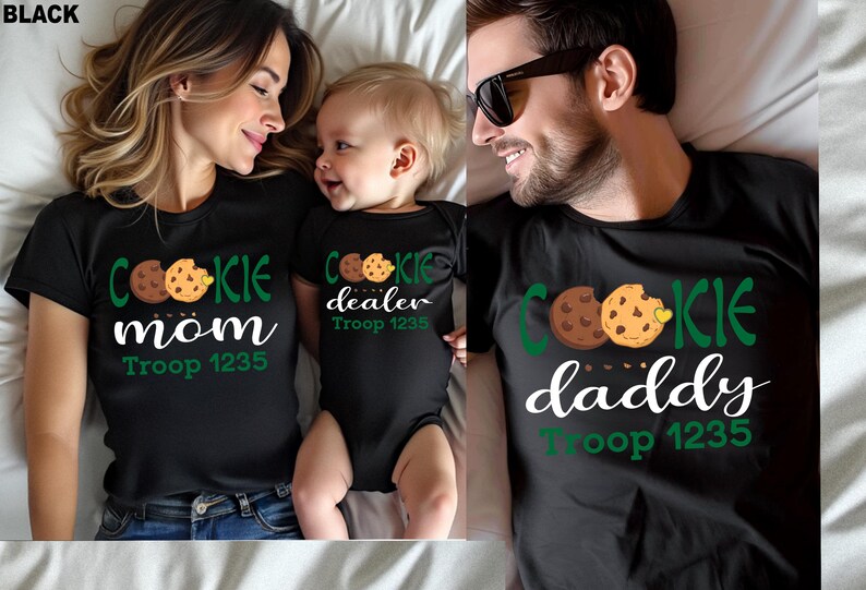 May include: Black t-shirts and a onesie with cookie-themed graphics. The shirts say "Cookie Mom" and "Cookie Daddy", and the onesie says "Cookie Dealer". All items include "Troop 1235".