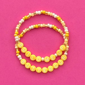 May include: Two yellow beaded bracelets with the words "Build Me Up" and "Buttercup" spelled out in white letters.