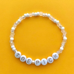 May include: White beaded bracelet with the word "TOE PICK" spelled out in silver letters.
