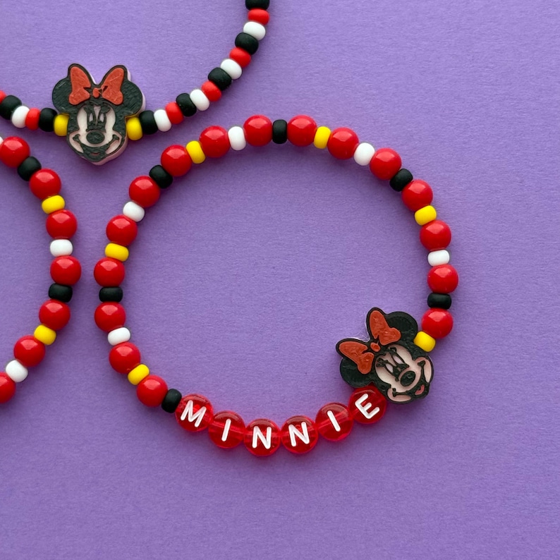 May include: Three beaded bracelets with a Minnie Mouse theme. The bracelets feature red, black, yellow, and white beads. One bracelet spells out "Minnie" in red beads. Each bracelet has a Minnie Mouse charm.