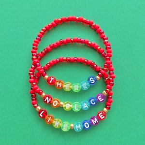 May include: Three red beaded bracelets with the words "There's No Place Like Home" spelled out in rainbow coloured beads.