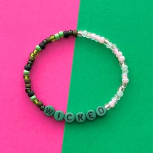 May include: A green and white beaded bracelet with the word "WICKED" spelled out in black letters on green beads.