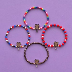 May include: Four colorful beaded bracelets with a Mickey Mouse ice cream charm. The bracelets are red, white, and blue, rainbow, and brown.