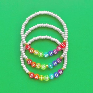 May include: Three white beaded bracelets with the words "Somewhere Over The Rainbow" spelled out in rainbow coloured beads.
