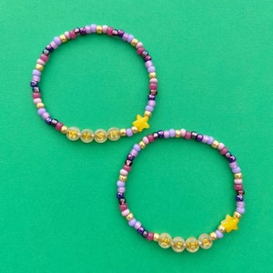 May include: Two beaded bracelets with gold star charms and the names "WISH" and "ASHA" spelled out in gold letters.