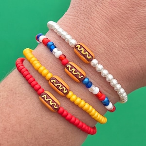 May include: Four bracelets with hot dog charms. The bracelets are red, yellow, white, blue, and white pearl beads.