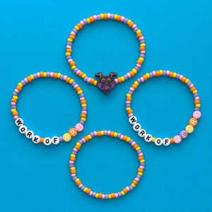 May include: Three colorful beaded bracelets with the words "Work of Art" and "Work of the Heart" spelled out in white letters.