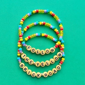 May include: Three colourful beaded bracelets with the words "Follow the Yellow Brick Road" spelled out in black letters on the beads.