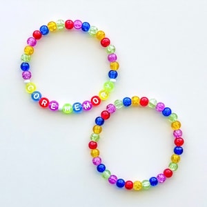 May include: Two colourful beaded bracelets. One bracelet spells out "CORE MEMORY" with white letter beads. The other bracelet is made of assorted coloured beads. The beads are red, yellow, green, blue, and purple.