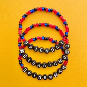 May include: Three black beaded bracelets with red and blue beads. The bracelets spell out "Spiderman", "Friendly", and "Neighborhood".