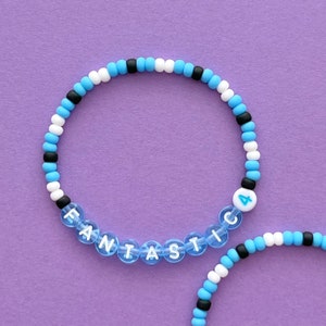 May include: Two beaded bracelets, one with the word "FANTASTIC" spelled out in white letters on blue beads and the other with alternating black, white, and blue beads and a blue bead with the number "4" in white.