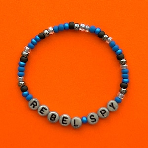 May include: A blue and silver beaded bracelet with the word "REBEL SPY" spelled out in silver beads.