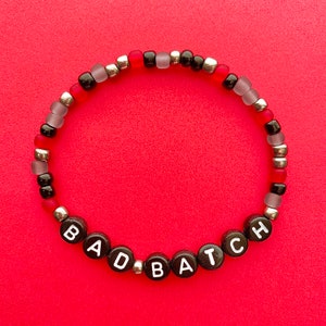 May include: A black beaded bracelet with red and silver beads spelling out the word "BAD BATCH".