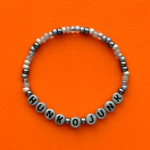 Könnte beinhalten: Ein silbernes und graues Perlenarmband mit dem Wort "HUNK O JUNK" in schwarzen Buchstaben.