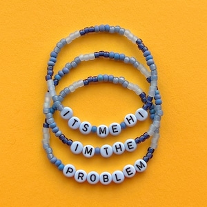 May include: Three blue and white beaded bracelets with the words "It's Me Hi I'm The Problem" spelled out in white beads.