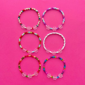 May include: Six colorful beaded bracelets with snowflake charms. Each bracelet features a different color combination of beads, including red, green, blue, pink, and white.