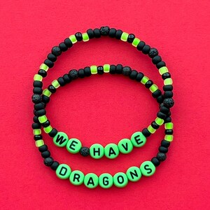 May include: Two beaded bracelets with the text "WE HAVE DRAGONS" in green letters. The bracelets are made of black and neon green beads, with a red background.
