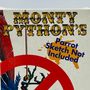 May include: A VHS tape cover for Monty Python's Parrot Sketch Not Included. The cover features a red circle with a diagonal line through it, and a parrot with colorful feathers is depicted inside the circle. The text "Parrot Sketch Not Included" is written in yellow and black letters on a white background. The quote "It's the best collection that I almost appeared in." is attributed to "Norwegian Blue Parrot".