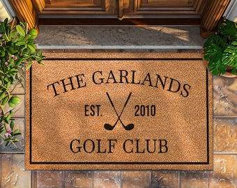 May include: A brown coir doormat with black text that reads "The Garlands Est. 2010 Golf Club" with a graphic of two crossed golf clubs.