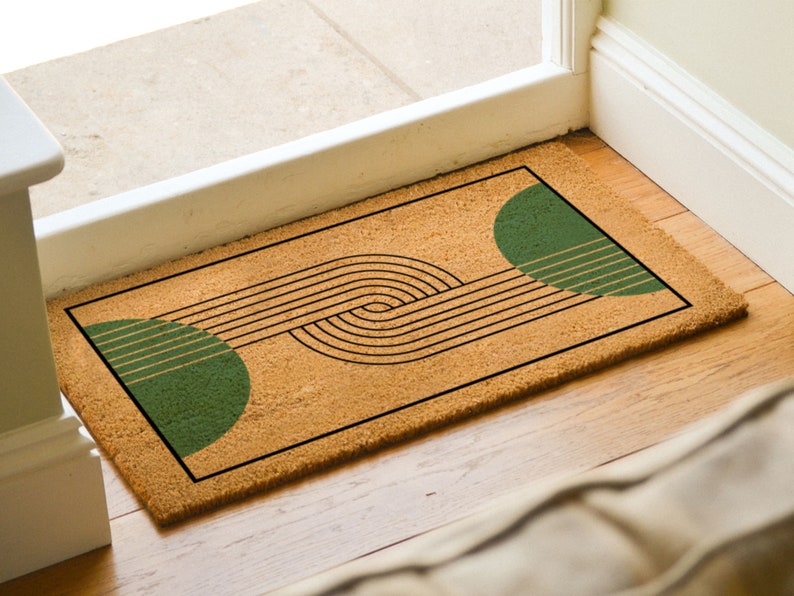 May include: A brown coir doormat with a geometric design featuring black lines and two green half circles.