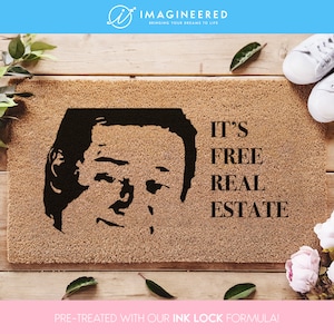 May include: A brown doormat with a black and white image of a man's face and the text "IT'S FREE REAL ESTATE".