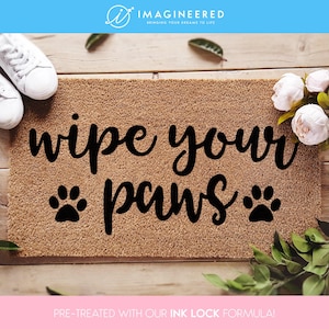 Könnte beinhalten: Eine braune Kokosmatte mit dem Text "wipe your paws" in schwarzer Kursivschrift. Zwei schwarze Pfotenabdrücke befinden sich auf beiden Seiten des Wortes "paws".