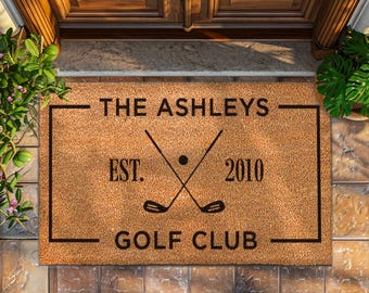 May include: A brown coir doormat with the text "The Ashleys Golf Club Est. 2010" and a graphic of two crossed golf clubs with a golf ball.