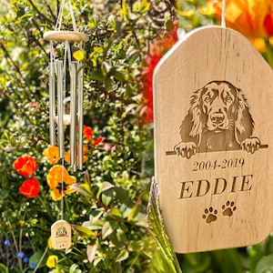 以下が含まれることがあります： 「2004-2019 EDDIE」と名前の下に肉球の跡が刻まれた、パーソナライズされた銘板付きの木製風鈴。風鈴には、犬の頭が上部から覗いている彫刻が施されています。