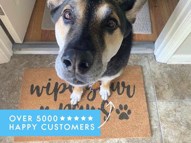 Pu&ograve; includere: Un cane marrone e nero con una zampa bianca &egrave; in piedi su uno zerbino marrone con il testo "Wipe your paws" in lettere nere. Lo zerbino ha un'impronta di zampa nera nell'angolo in basso a destra. Il testo "OVER 5000 ***** HAPPY CUSTOMERS" &egrave; in testo bianco su sfondo blu.