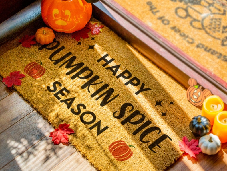 May include: A brown doormat with the text "Happy Pumpkin Spice Season" in black lettering. The doormat is decorated with fall-themed elements, including pumpkins, leaves, and stars.