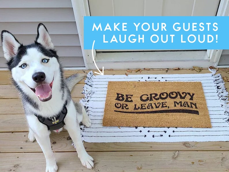 May include: A brown doormat with the text "Be groovy or leave, man" in black lettering. A husky dog with blue eyes is sitting on a wooden deck in front of the doormat.