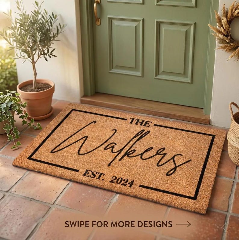 May include: A rectangular doormat made of natural fibers, featuring the name "The Walkers" in elegant script, with "EST. 2024" below. The mat is framed in black and rests in front of a green door.