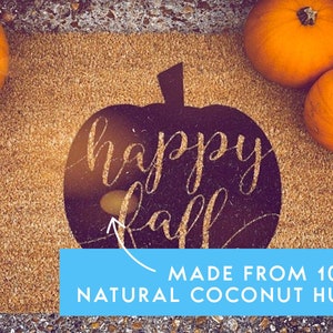 Puede incluir: Una alfombra de bienvenida marr&oacute;n con una silueta de calabaza negra que dice "happy fall" en purpurina dorada. La alfombra est&aacute; hecha de 100% fibra de coco natural. Hay tres calabazas naranjas en la esquina superior derecha de la alfombra.